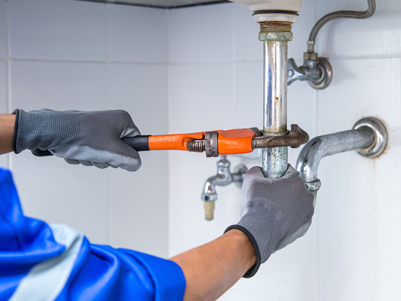 Technician plumber using a wrench to repair a water pipe under the sink.