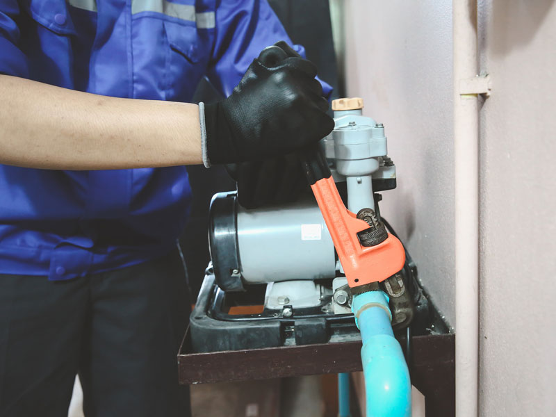 Technician plumber using a wrench to repair a water pump pipe.