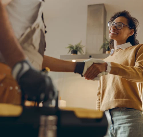 Close up of male handyman shaking hands with happy female client while standing at home kitchen